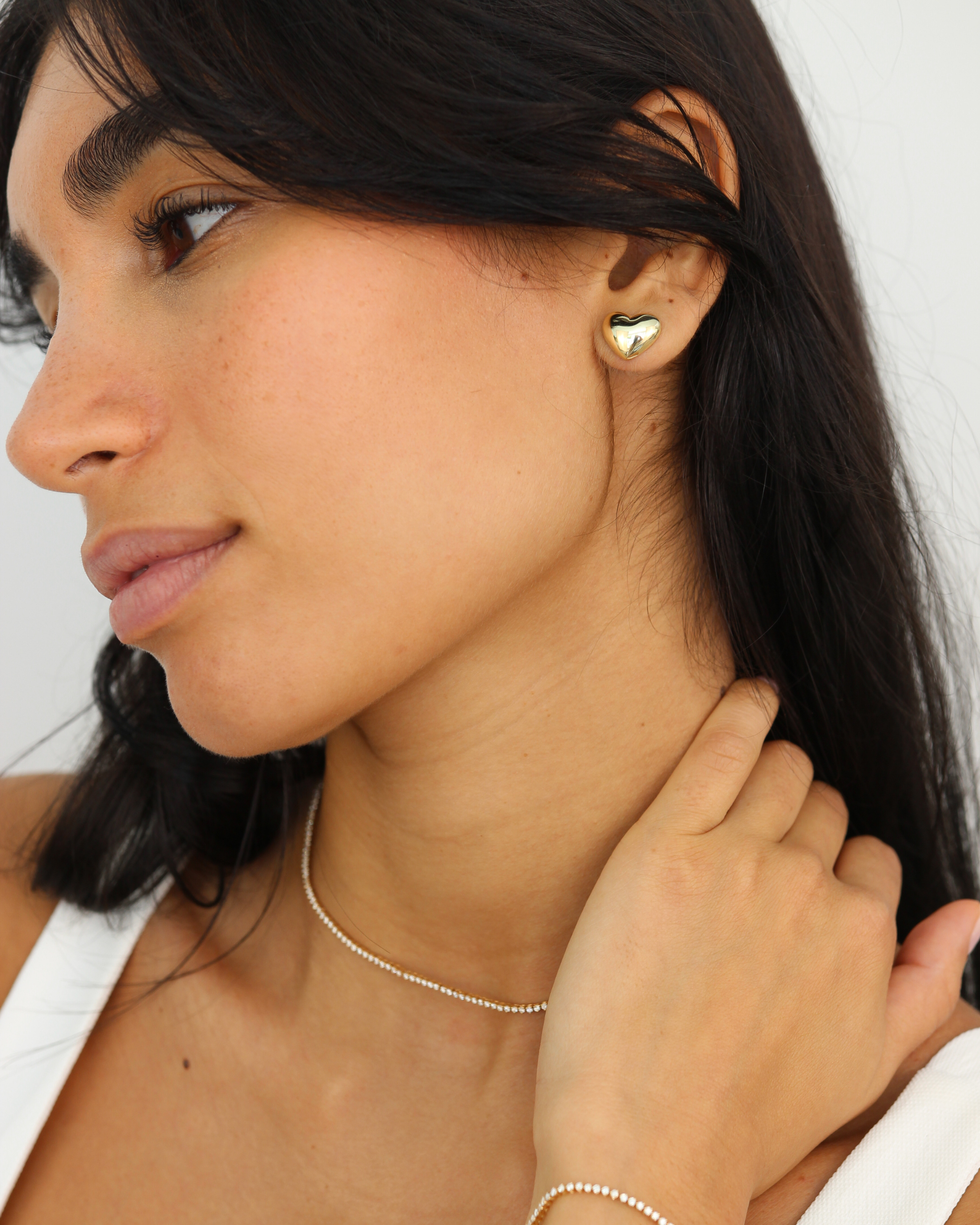 Woman wearing a gold heart-shaped earring on a white background