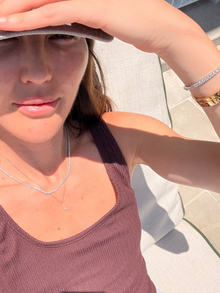 Woman wearing a brown tank top and diamond necklace, sitting outdoors.
